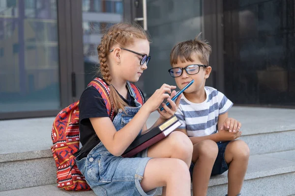 Duas crianças em óculos com livros e mochila digitando no telefone Imagem De Stock