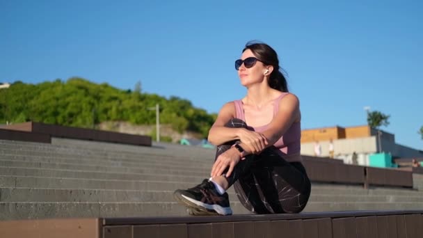 Jonge fitnessvrouw klaar met rennen, zitten en muziek luisteren — Stockvideo