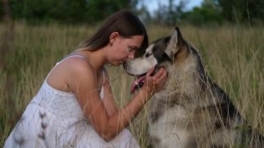 Alaska Malamute köpeğine sarılıp öpen mutlu bir kadın.