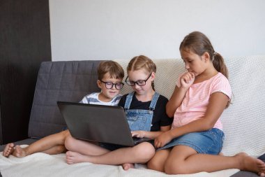 Evde bilgisayar ve telefon kullanan üç beyaz çocuk.