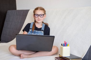  Gözlüklü, laptopla evde ders çalışan, beyaz, mutlu, kızıl saçlı bir kız.