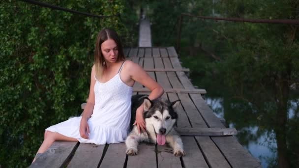 Happy woman pet alaskan malamute dog on suspension bridge — Vídeo de Stock