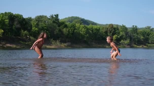 Радостный счастливый мальчик и девочка играют и брызгают друг друга в воду — стоковое видео