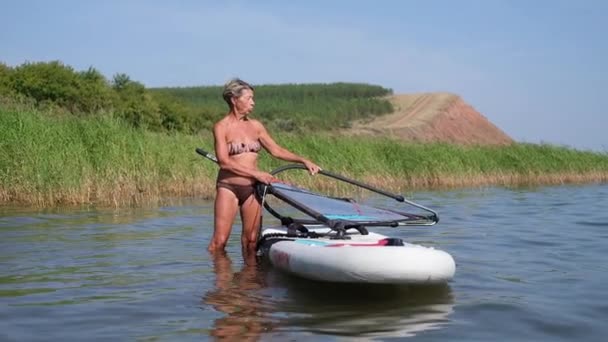 Mujer mayor activa en paseo traje de baño ir con windsurf en el agua — Vídeo de stock