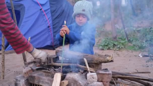 Kleine blanke jongen zit bij een kampvuur in het bos — Stockvideo