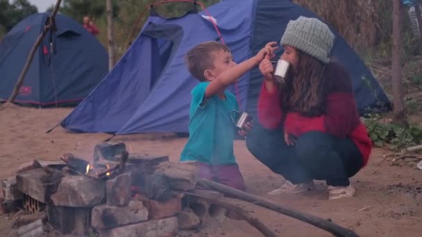Két gyerek forró csokit iszik a tábortűznél az erdőben. — Stock videók
