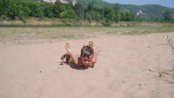 Радісний щасливий хлопчик лежить і грає в пісок — стокове відео