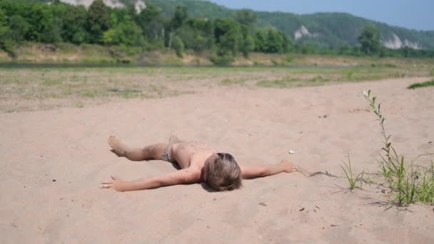 Sällsynt utsikt över glad pojke som ligger och leker i sand — Stockvideo