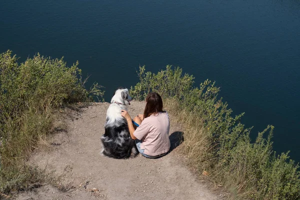 Woman sit with australian shepherd dog on river bank outdoor. — Stock Photo, Image