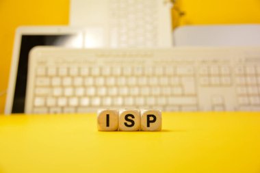 ISP kelimesi, bilgisayarlı ve klavyeli sarı bir arkaplan önünde gerçek ahşap zarlarla yazılmış.
