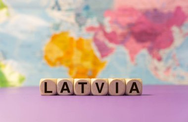 Letonya kelimesi mor bir arkaplan ve coğrafi harita önünde tahta zarlarla yazılmış.