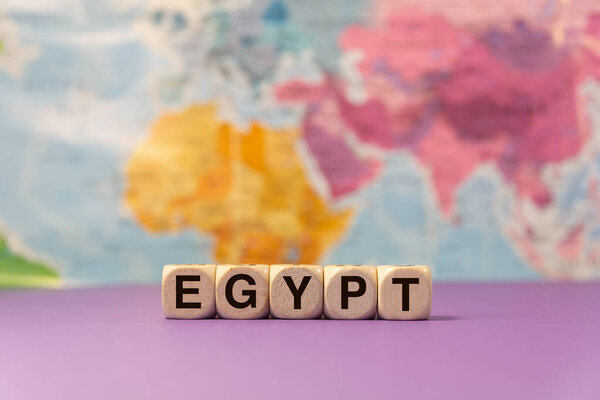 The word Egypt written with wooden dices in front of a purple background and a geographic map