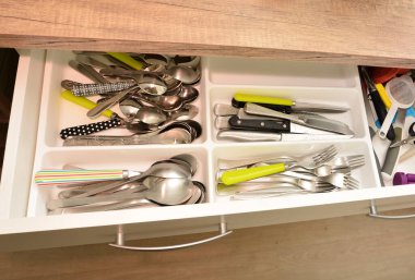 Kaşıklar, çatallar, bıçaklar ve diğer malzemelerle dolu açık bir mutfak çekmecesi.