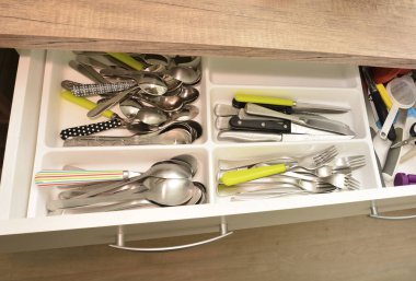 Kaşıklar, çatallar, bıçaklar ve diğer malzemelerle dolu açık bir mutfak çekmecesi.