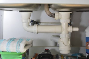 Temizlik ürünleri ve beyaz pastik sifonlarla lavabonun altındaki mutfak dolabının manzarası