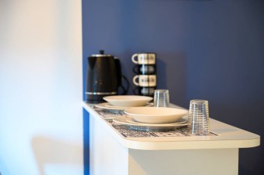 Modern minimalist beyaz tezgah, siyah kahve makinesi ve modern mutfakta mavi duvara karşı istiflenmiş kahve fincanları.