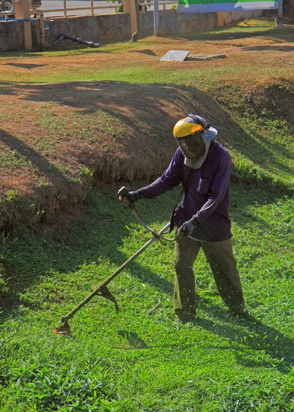 Homem está aparando grama ao ar livre — Fotografia de Stock