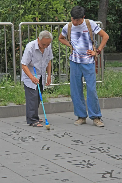 Old man is writing Han characters on the ground with brush and water — Stock Photo, Image