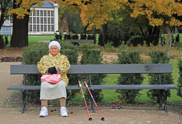 Oude vrouw met krukken is zittend op een bankje — Stockfoto