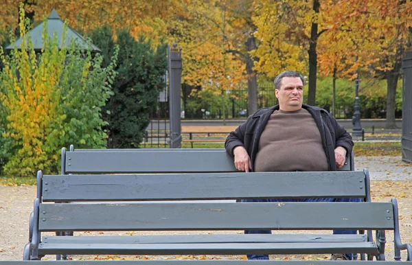 Fet man sitter på en bänk i parken i Warszawa — Stockfoto