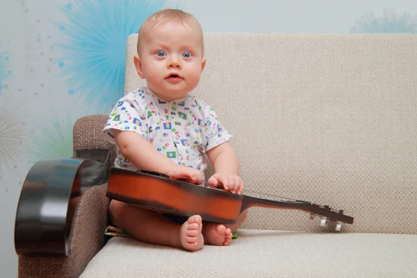 Bebé tratar de tocar la guitarra en el sofá — Foto de Stock