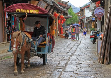 man is driving horse-drawn vehicle  in Lijiang, China