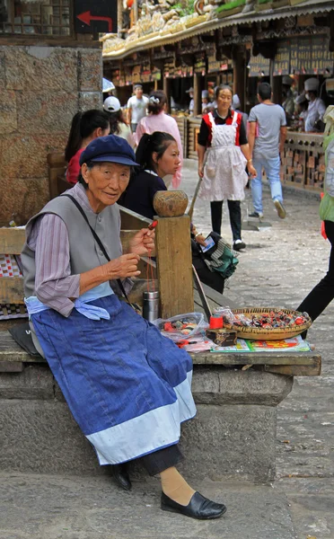 Old woman is selling handmade souvenirs on the street in Lijiang, China — Stok fotoğraf