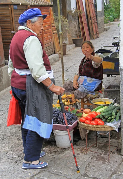 Woman-seller of vegetables is talking with her friend on the street in Lijiang, China — Stock Fotó