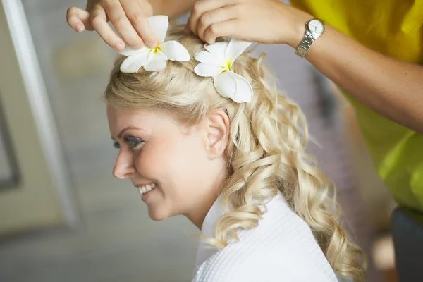 Beautiful, cute blond bride doing hair with flowers before weddi