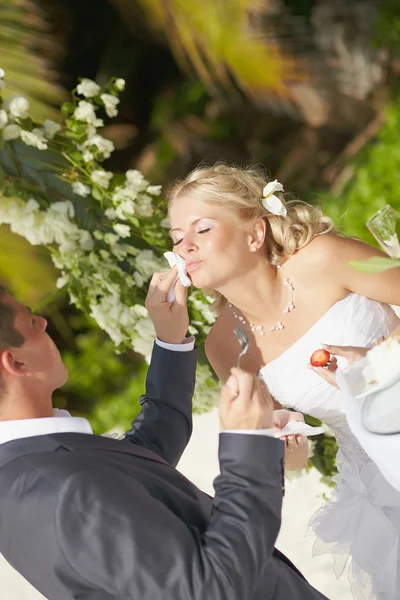 Bella coppia mangiare torta nuziale durante il matrimonio tropicale cerem — Foto Stock