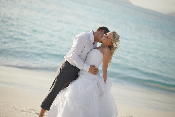 Beautiful young couple kissing on sunset, standing barefoot on b