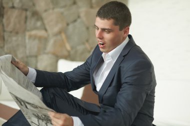 Yakışıklı genç adam siyah takım elbiseli sabah gazetesi okuyor.