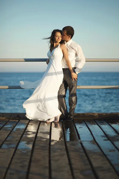 Preciosa pareja de boda de pie en el muelle bajo aerosol, salpica un — Foto de Stock