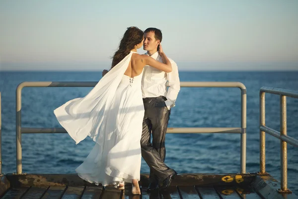 Wunderschöne Hochzeitspaar küsst sich auf Pier unter Gischt, spritzt ein — Stockfoto