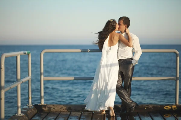 Wunderschöne Hochzeitspaar küsst sich auf Pier unter Gischt, spritzt ein — Stockfoto