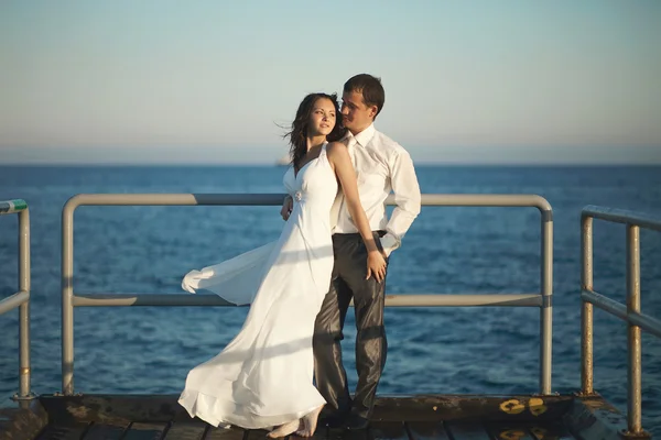 Prachtvolles Hochzeitspaar steht auf Pier unter Gischt, spritzt ein — Stockfoto