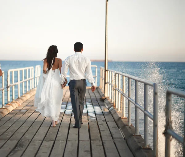 Prachtvolles Hochzeitspaar spaziert durch Pier, Spritzer und Tropfen — Stockfoto