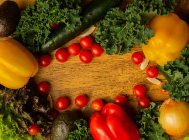 Tahta bir masada taze olgun sebzeler, domatesler, salatalıklar, avokadolar, marul, lahana, sarımsak, dolma biber, sağlıklı yiyecekler.