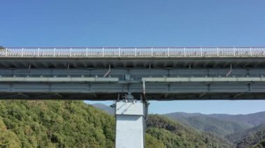 Yeşil çimlerle kaplı güzel tepelerin arasında kanyon üzerinde duran pitoresk kemer köprüsünün hava manzarası. Arabalar köprüden geçiyor. Gökyüzünün altında Rusya 'nın ünlü simgesi. 4K