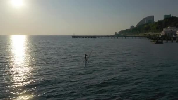 Sotchi, Russie-12 septembre 2020 : Prise de vue d'un homme en maillot de bain debout sur une planche à roulettes et nage en surfant sur la mer avec une pagaie pour des amis surfeurs sportifs de natation. Sotchi, Russie. plan aérien 4k drone — Video