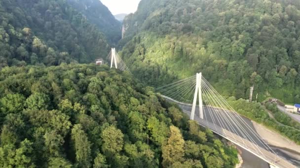 Vuelo lateral moderno puente de carretera por cable para el complejo Sochi Rusia tráfico de coches de autopistas suburbanas entre las altas montañas río desfiladero. Paisaje natural de pendientes verdes. Verano soleado. — Vídeo de stock