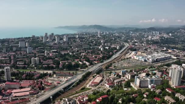 Εναέρια λήψη βίντεο. Πανοραμική θέα του κέντρου της πόλης του Σότσι. Υψηλό κτίριο σε φόντο πράσινων βουνών. Όχι άνθρωποι. Μπλε καθαρός ουρανός. κάμερες σε κίνηση — Αρχείο Βίντεο