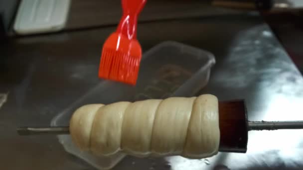 Las manos envuelven los palos de masa en un palo de madera. Nacional checa trdelnik dulce delicadeza.Tradicional checo y húngaro panadería dulce para hornear. — Vídeo de stock