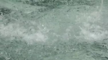 Damlaların ve fıskiyedeki su damlalarının yakın görüntüsü. Çeşmedeki mavi su parıldıyor ve parlıyor..