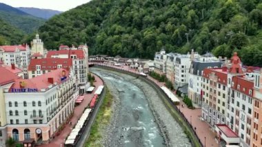 Rosa Khutor tatil köyü, belediye binası, yaya köprüsü, Rathaus ve güneşli bir günde merkez meydan manzarası. Roza Khutor. Dağlar. Güneşli bir gün. Oteller. Mzymta Nehri. Krasnaya polyana. 