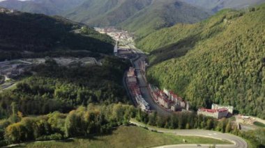 Rosa Khutor tatil köyü, belediye binası, yaya köprüsü, Rathaus ve güneşli bir günde merkez meydan manzarası. Roza Khutor. Dağlar. Güneşli bir gün. Oteller. Mzymta Nehri. Krasnaya polyana. 