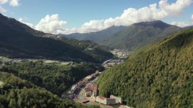 Rosa Khutor tatil köyü, belediye binası, yaya köprüsü, Rathaus ve güneşli bir günde merkez meydan manzarası. Roza Khutor. Dağlar. Güneşli bir gün. Oteller. Mzymta Nehri. Krasnaya polyana. 