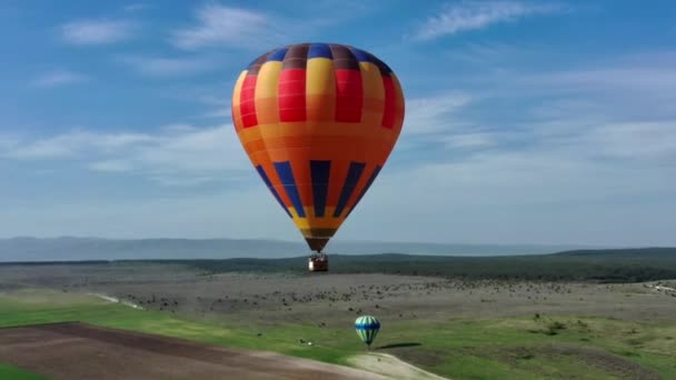 Mnohobarevný horkovzdušný balón s košíkem letí proti modré obloze. letecký pohled. — Stock video