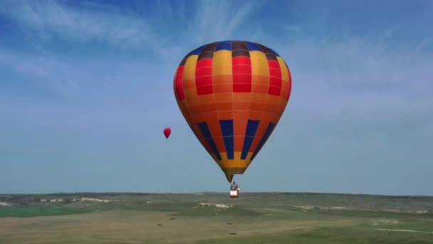 Um balão de ar quente multicolorido com uma cesta voa contra o céu azul. vista aérea. — Vídeo de Stock