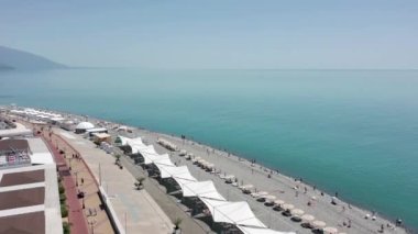 Hava videosu. Sochi 'nin olimpiyat seti. Kumsal. Karadeniz. Tatil sezonu. Modern şehir manzarası, Rusya 'nın popüler sahil beldesi. Şehir otelleri konut binaları olimpiyat parkı manzarası. 